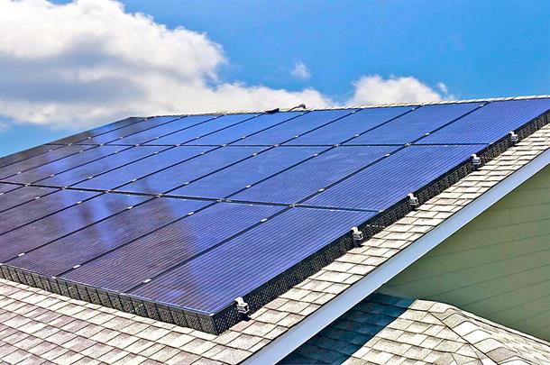 Solar panels installed on a sloped roof under a blue sky with clouds.